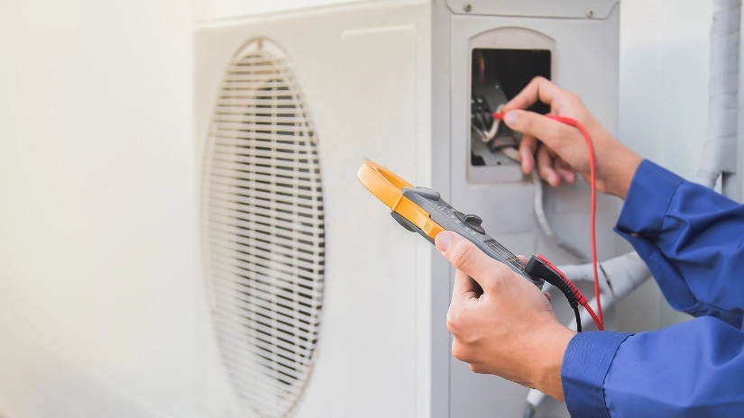 Coyco electrician hands troubleshooting with a multimeter in the back of an aircon on an air conditioning repair