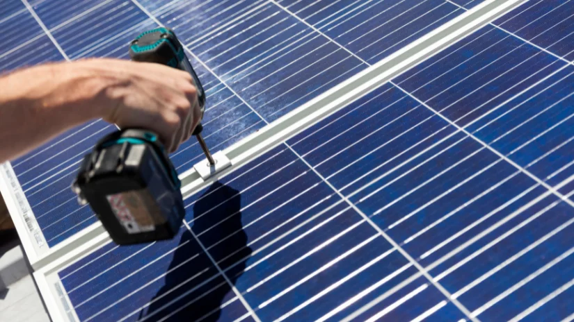 Hand holding drill to screw down solar panels for installation