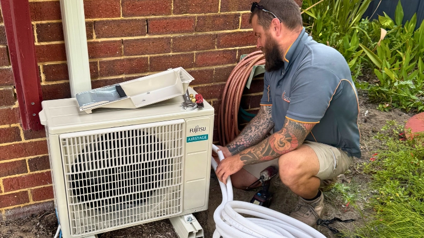 electrician from COYCO installing aircon unit outside near wall with pipes in foreground